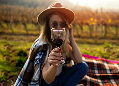 Young woman with hat sitting in vineyard with wine glass